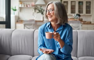 relaxed mature older adult grey haired woman drinking coffee relaxing on sofa at home.
